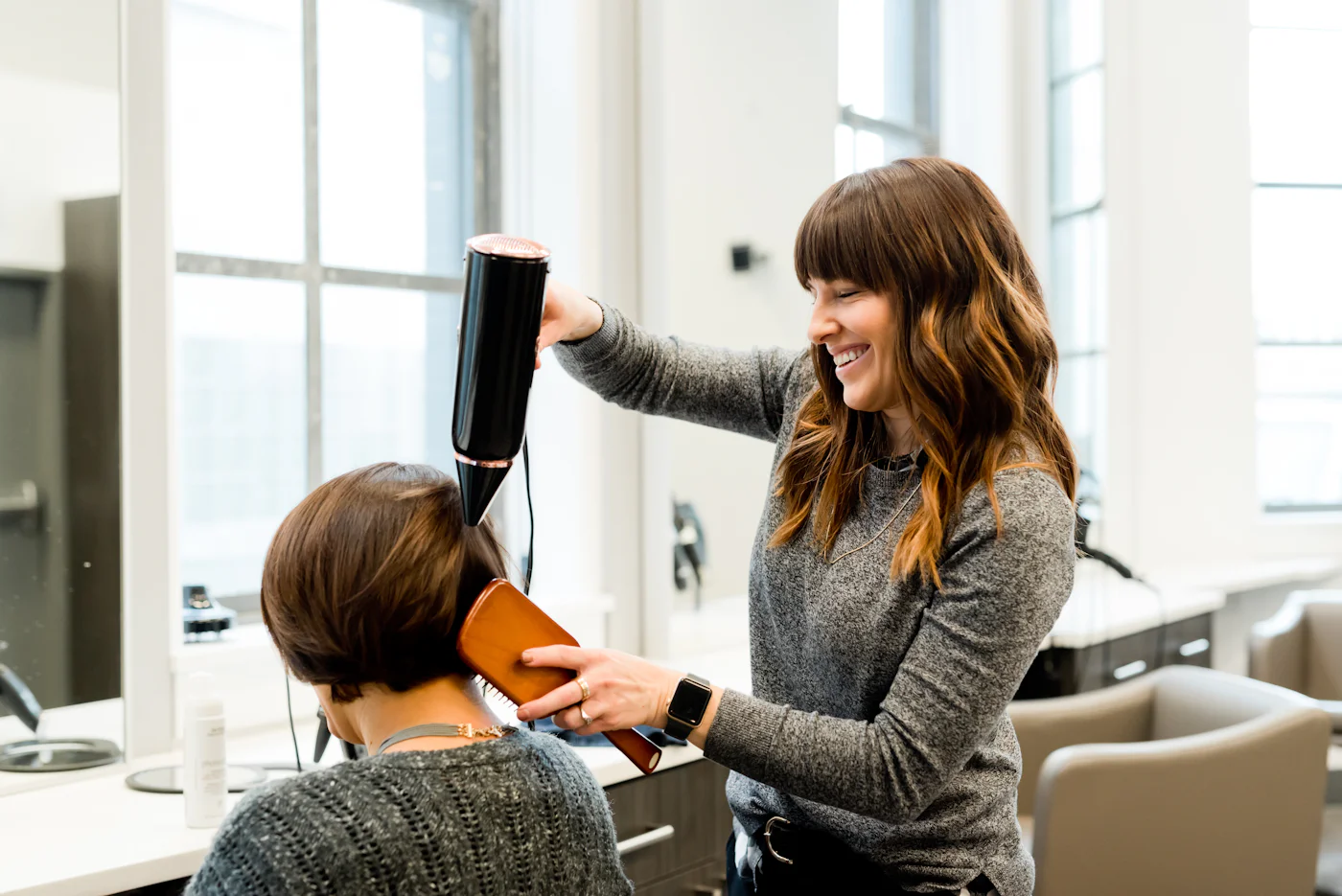 Friseurin föhnt einer Kundin die Haare und lacht